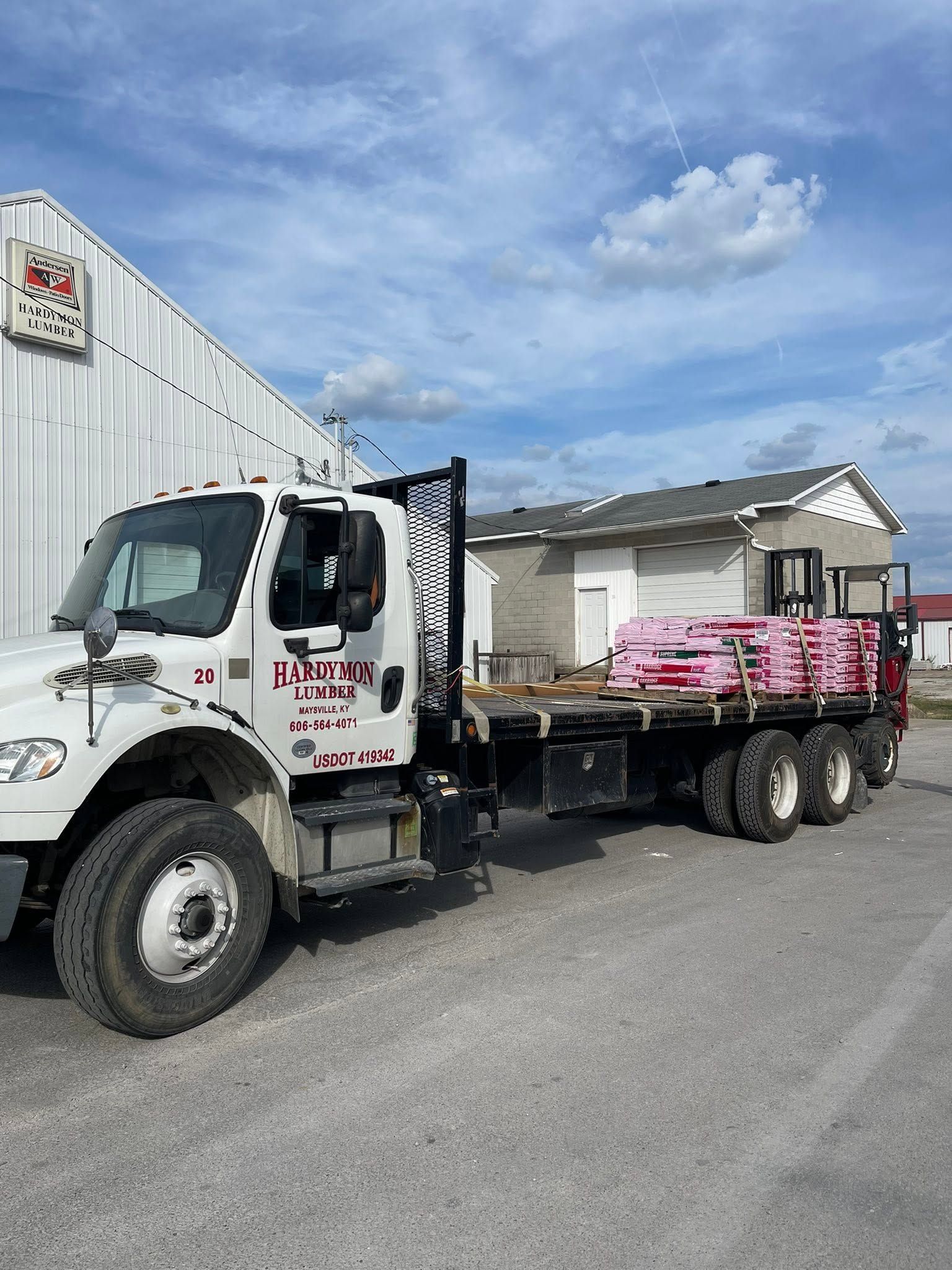 White flatbed truck loaded with pink materials parked on a street under a cloudy sky