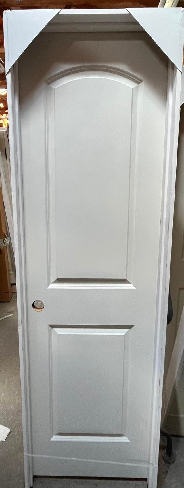 White paneled cabinet door with raised arch detail and lower inset panel, standing upright indoors.