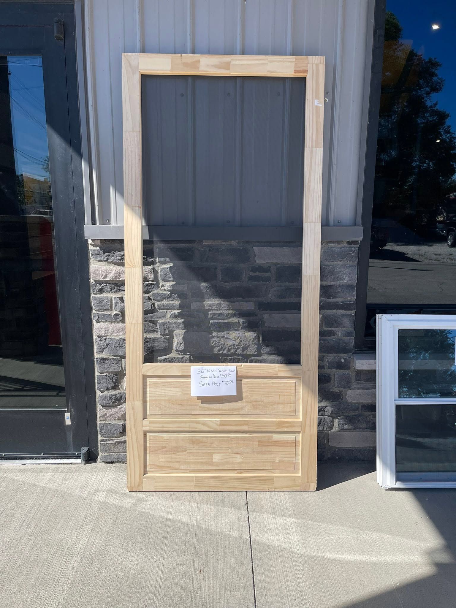Wooden-framed door panel leaning against a wall outside, with a small sign attached.