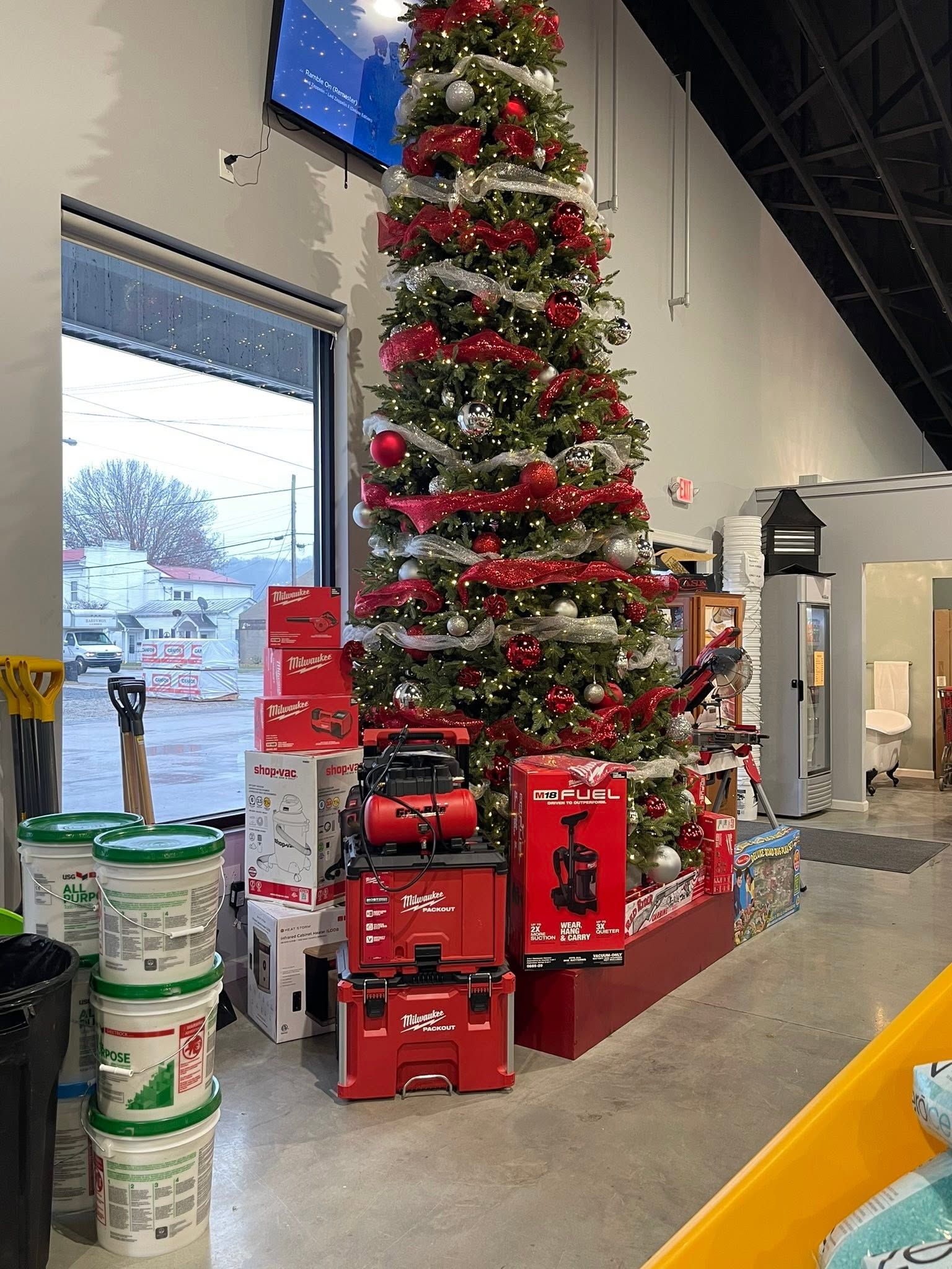 Tall decorated Christmas tree beside stacked red gift boxes in a store aisle