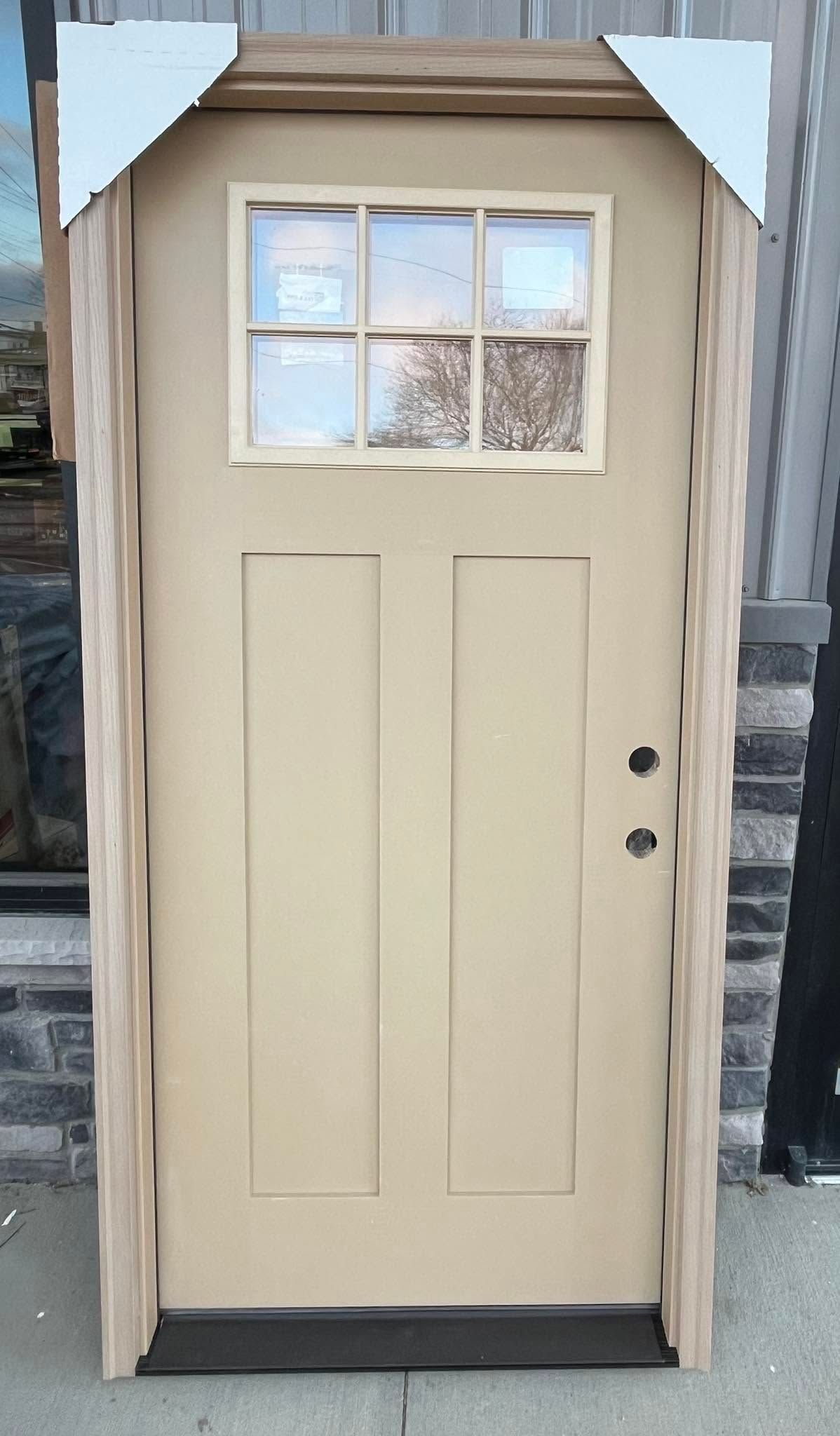Beige front door with four window panes, shown in a wooden frame outdoors.