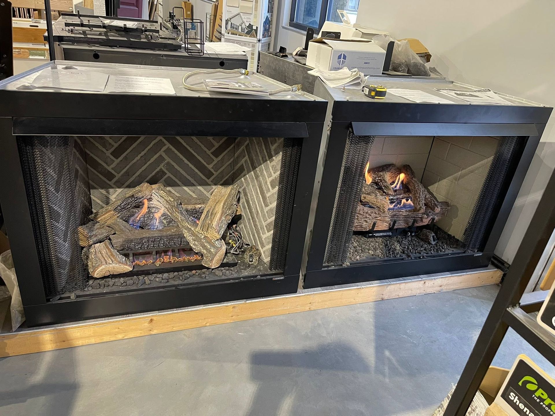 Two modern black-framed fireplaces with lit wood fires in a showroom or home interior