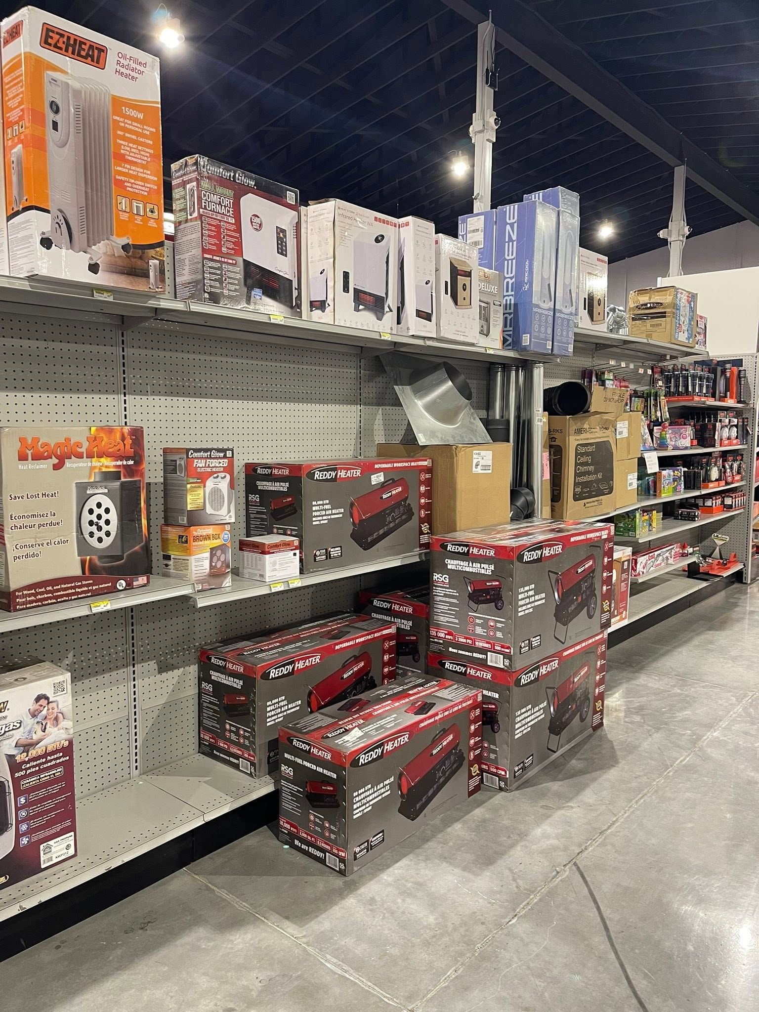 Store aisle with boxed power tools and hardware on shelves and floor displays under bright warehouse lighting