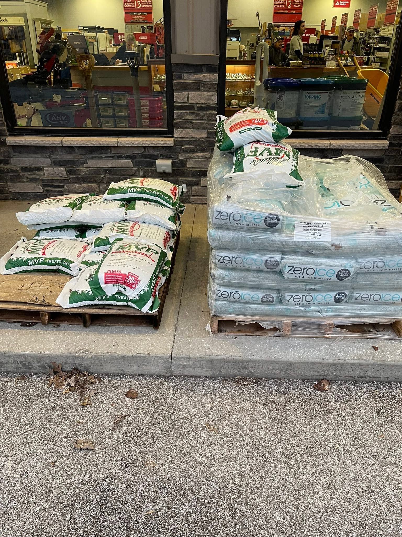 Pallets of bagged supplies stacked outside a store entrance, with products visible inside the window.