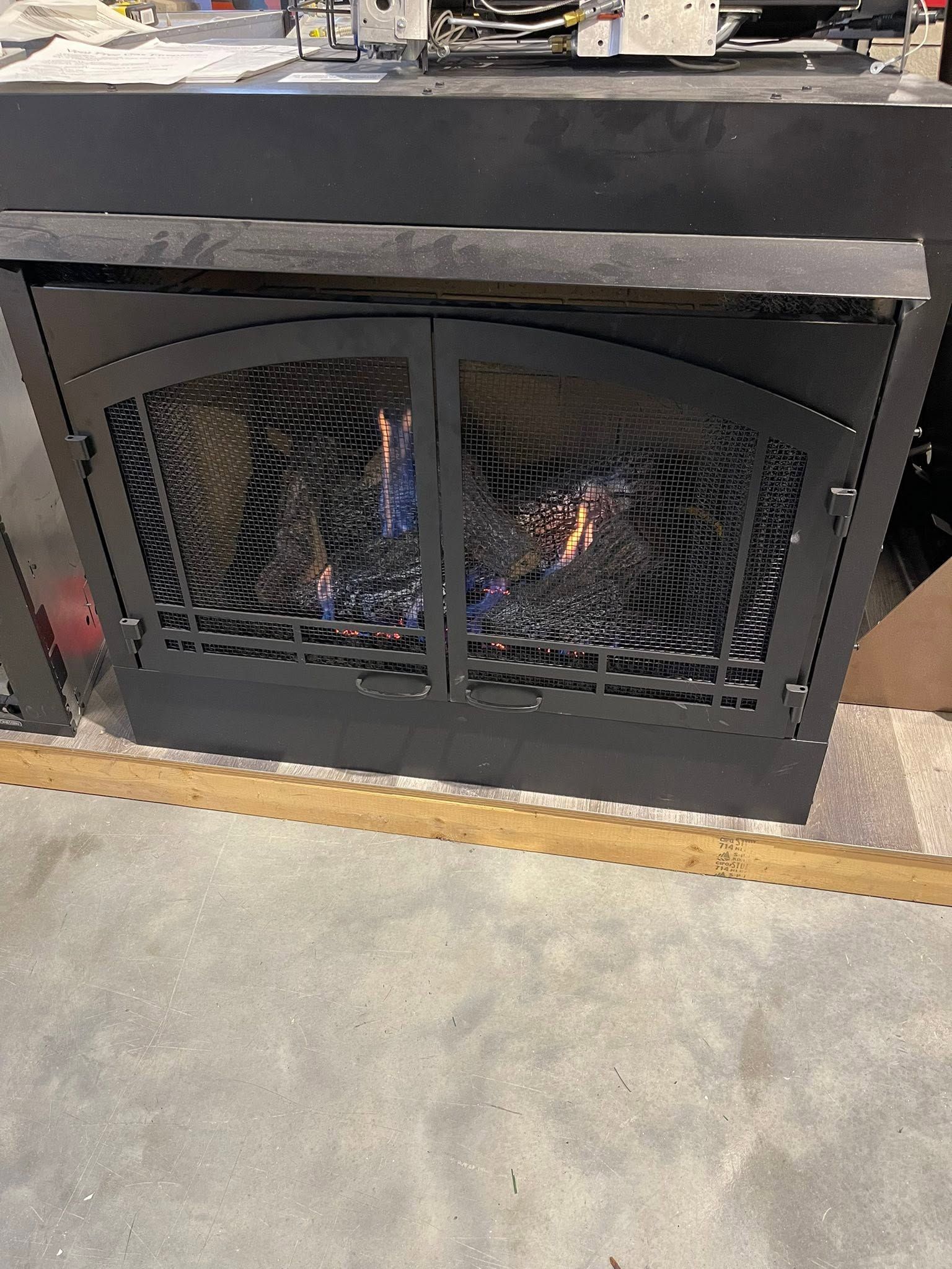 Black metal fireplace or fire pit with mesh doors and a small flame inside