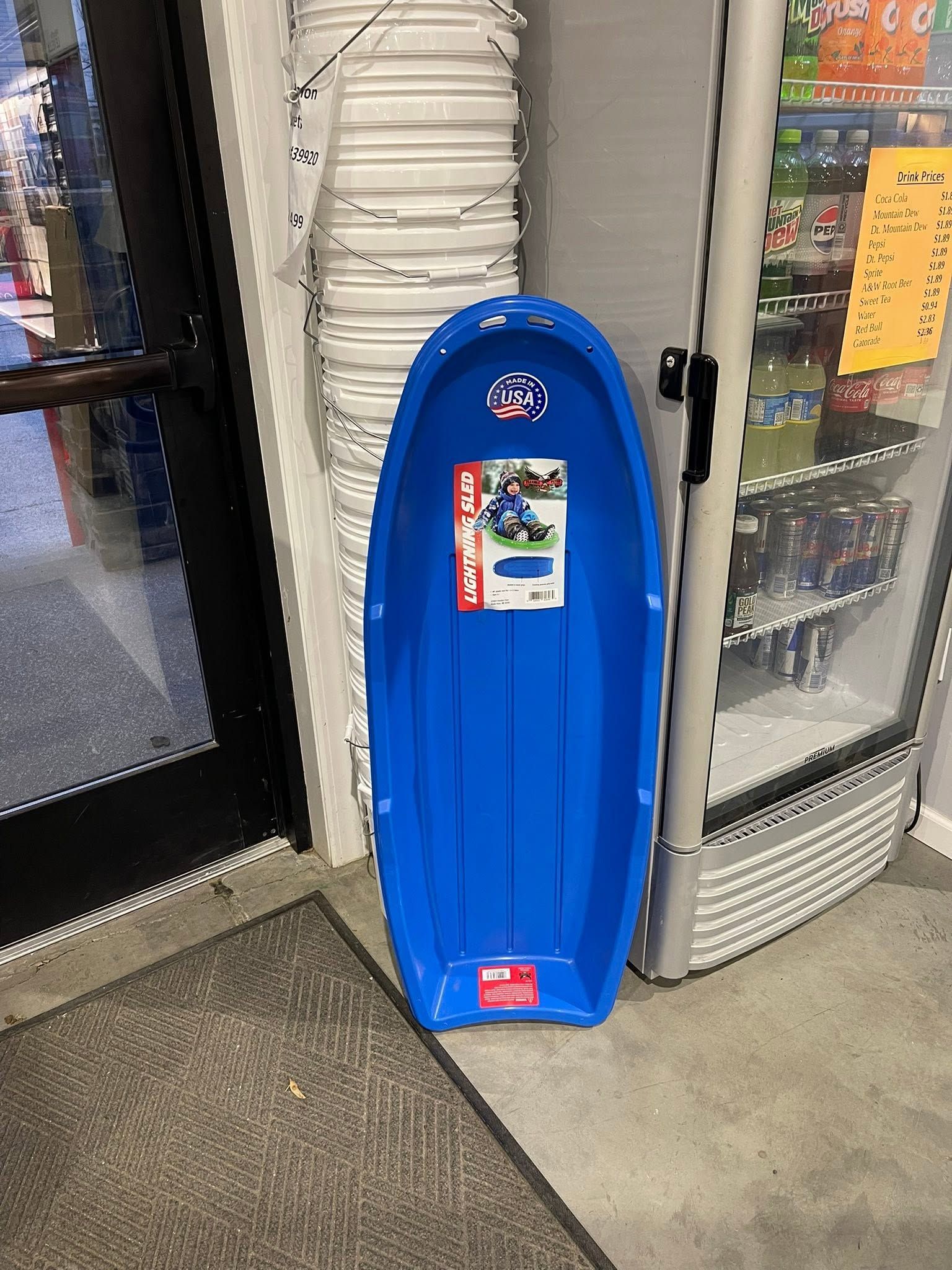 Blue sled standing upright by a store entrance next to stacked white trays and glass display cases