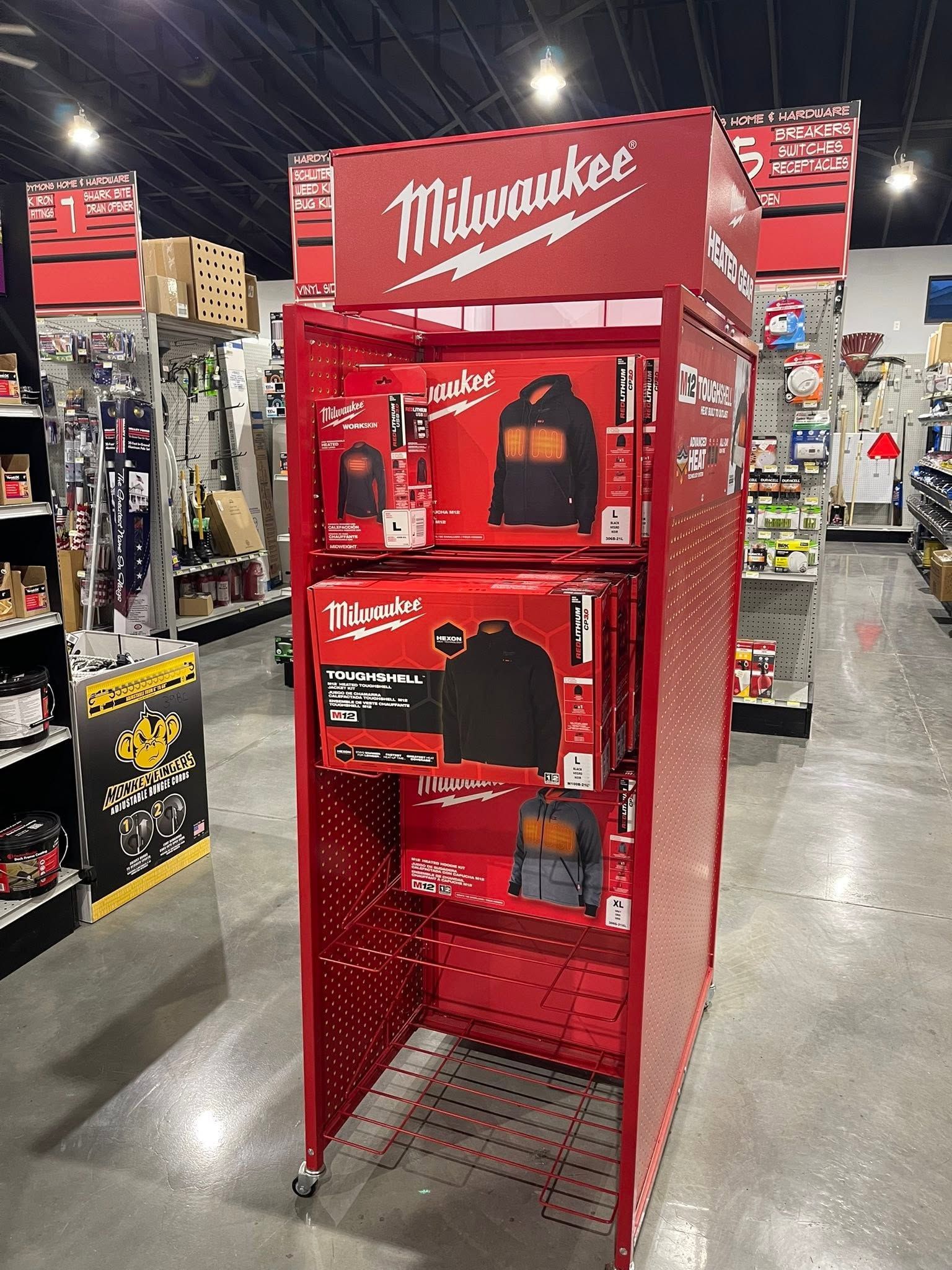 Red Milwaukee display rack in a store aisle with black shirts and red merchandise.