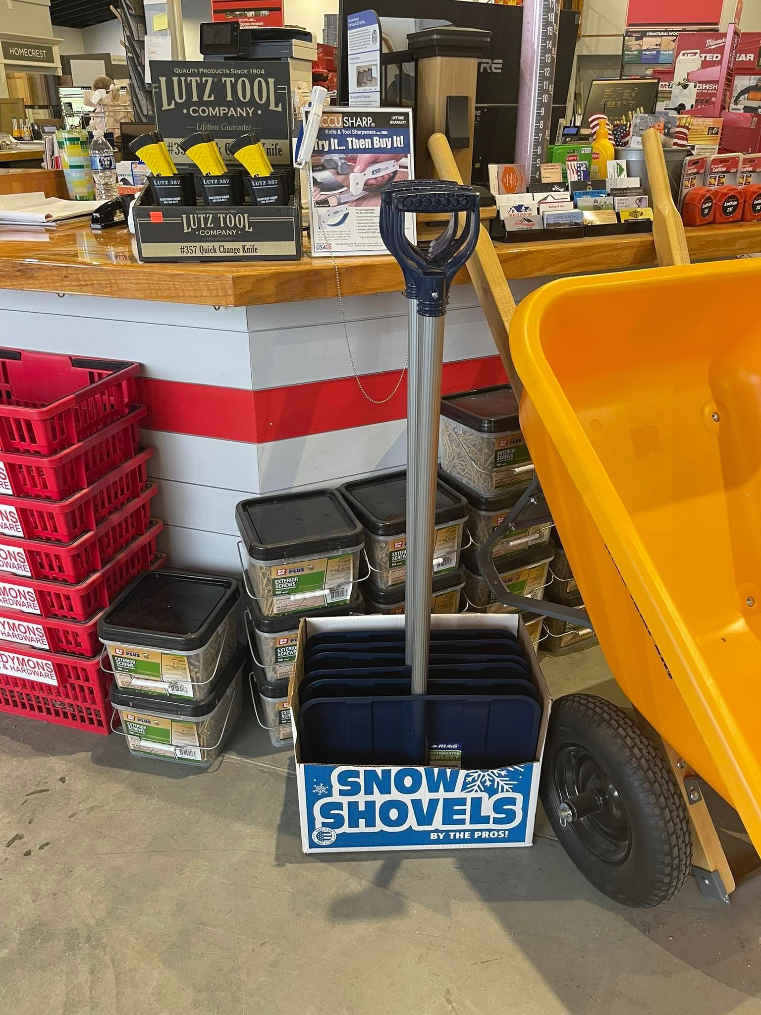 Snow shovels displayed in a store, with a yellow snow scoop and stacked boxes nearby