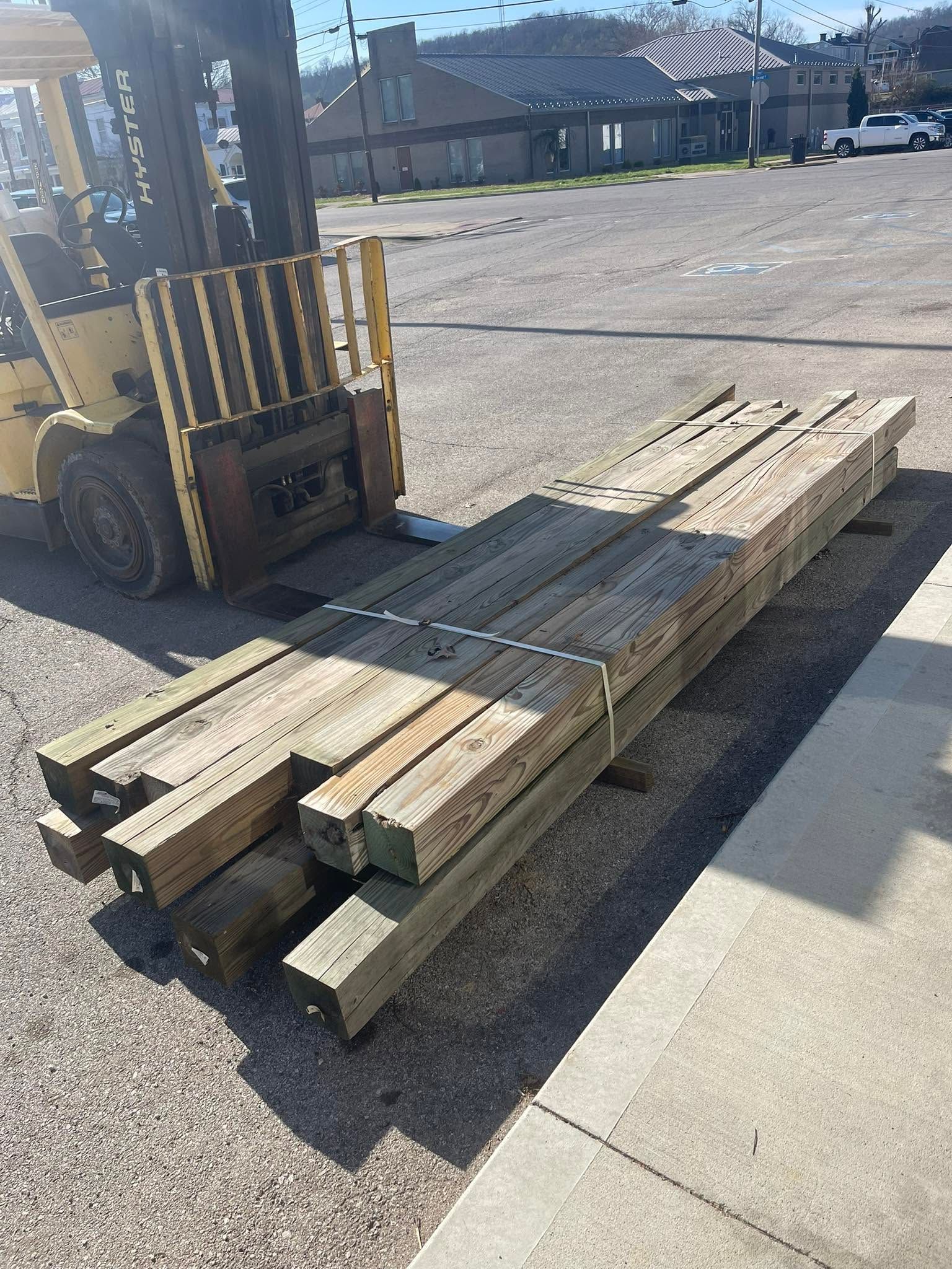 Stacked wooden planks beside a forklift in a sunlit parking lot