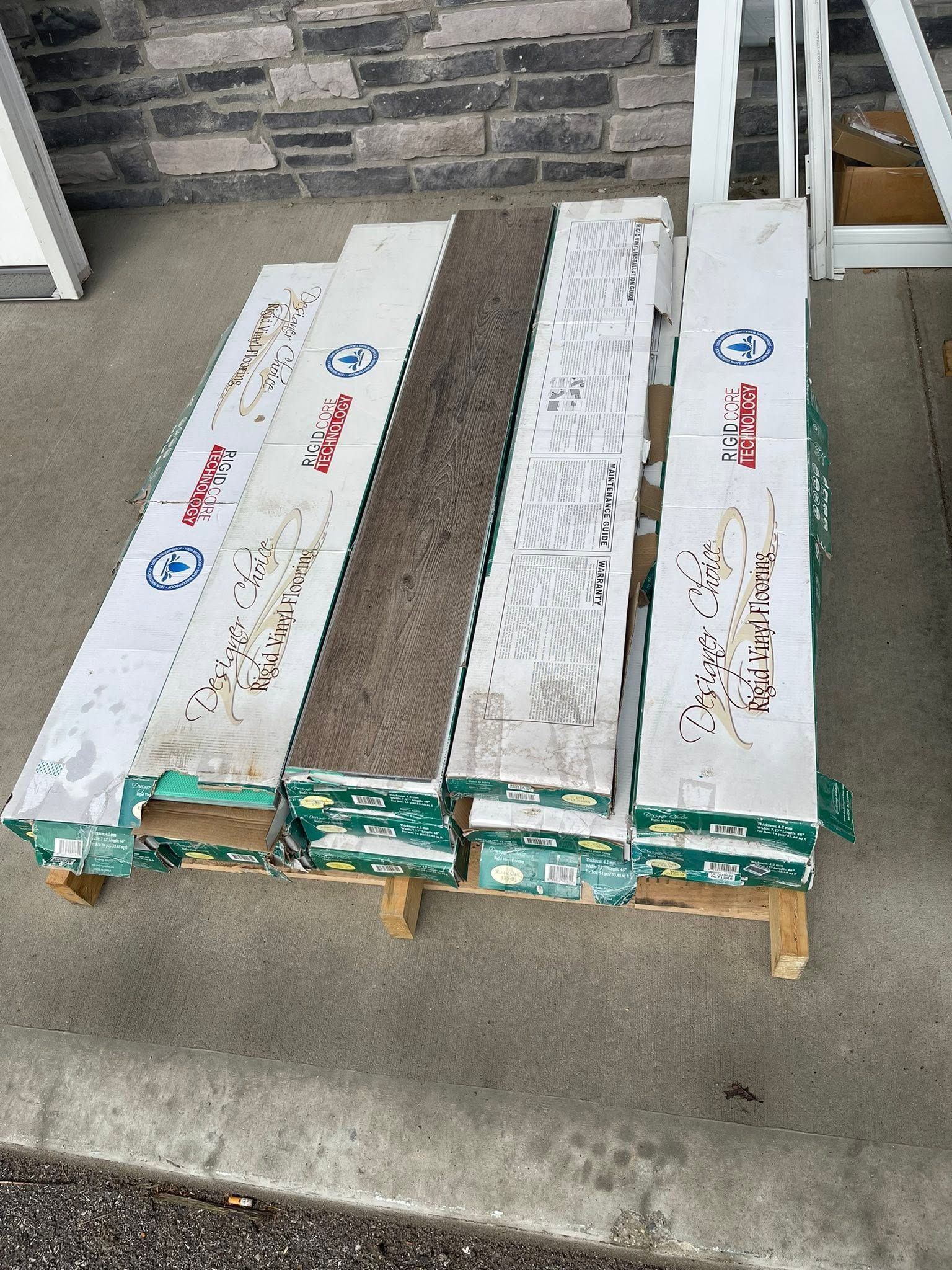 Three long white wrapped boards on a pallet outside a brick building.