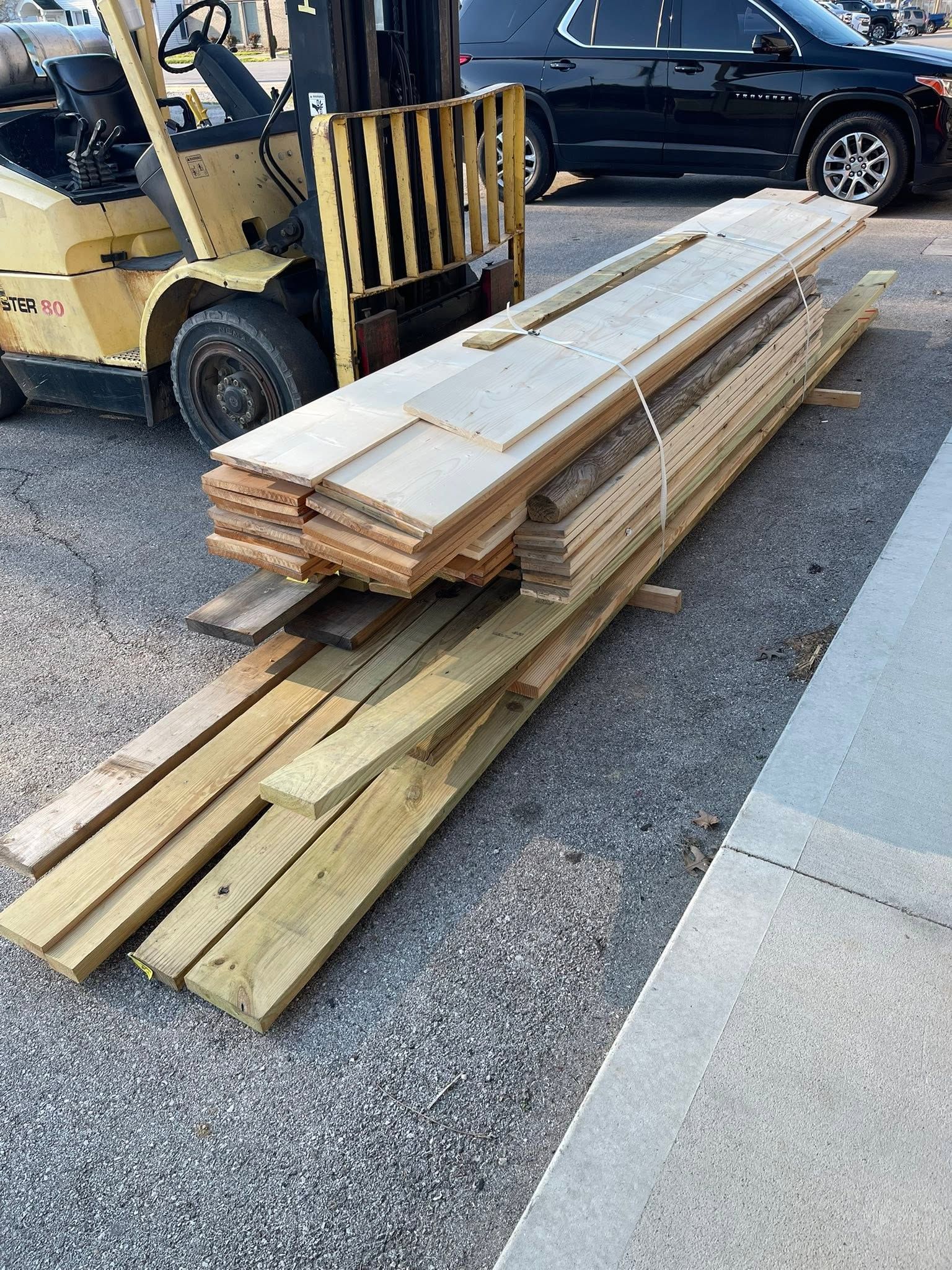 Stacked wooden planks on a pallet beside a forklift in a parking lot