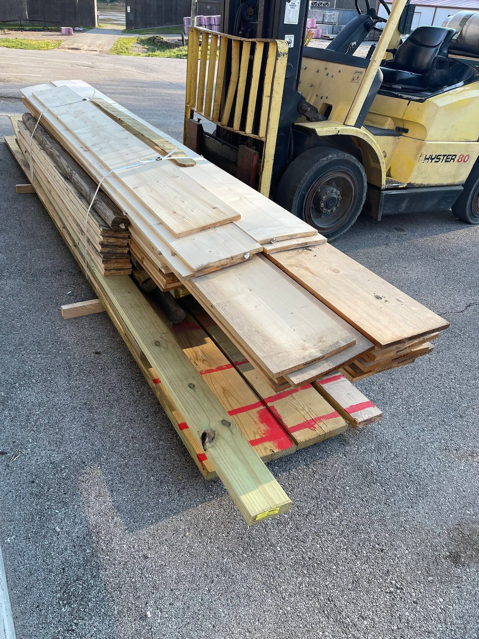 Stacked wooden planks and beams on a forklift in a gravel yard