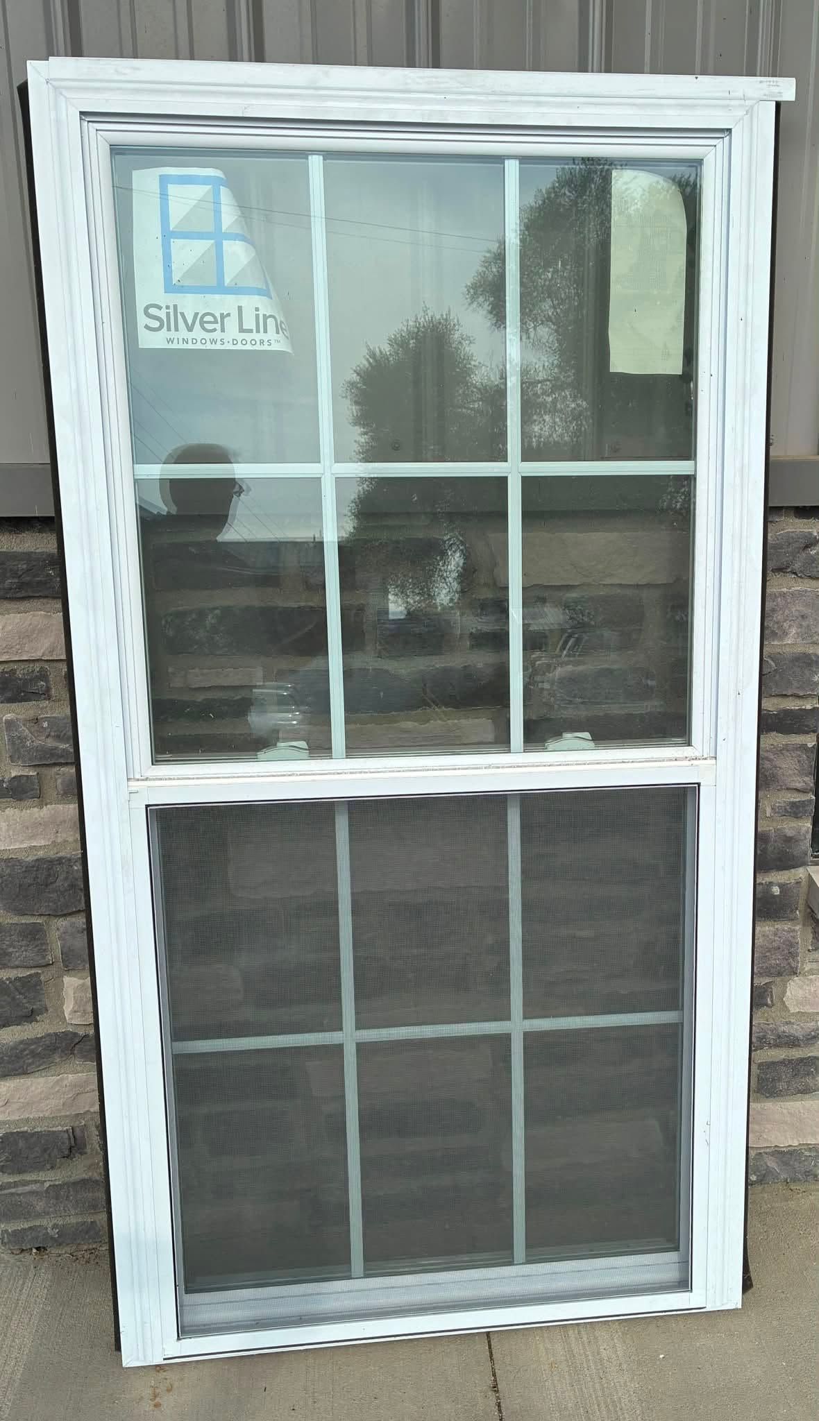 White-framed window with reflective glass in a stone wall, with a small sign in the upper left pane.