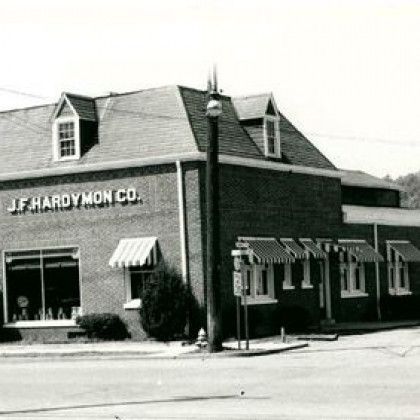 Black-and-white photo of J.F. Hardy Mon Co. storefront with awnings and a streetlight on a corner.