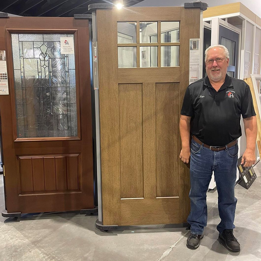 Man standing beside two wooden doors at an indoor display booth, one with a glass pane and one rustic brown panel door