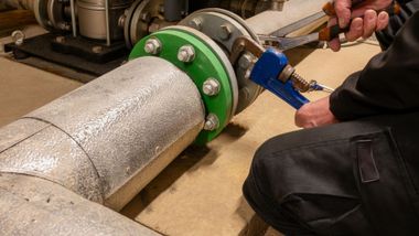 Worker tightening blue clamp on green pipe flange in an industrial setting Worker tightening blue clamp on green pipe flange in an industrial setting