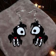 A pair of earrings featuring black skeleton ponies with white skull-like faces, white leg bones, and small red hearts.