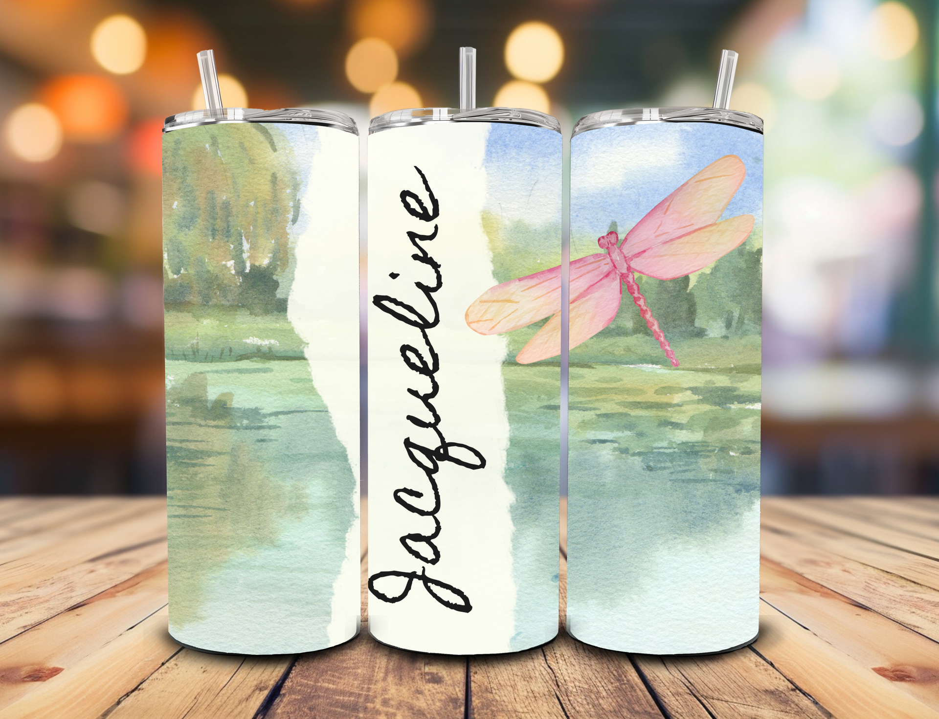 A custom tumbler featuring a watercolor landscape with a pink dragonfly and the name 