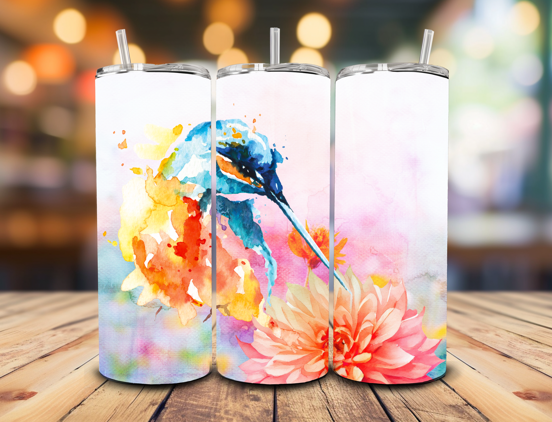 A sublimation tumbler with a watercolor painting of a blue hummingbird hovering over soft pink and orange flowers.