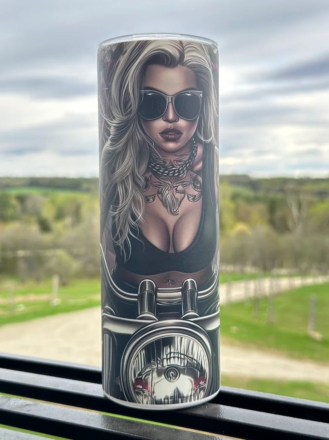 A cylindrical tumbler featuring a printed illustration of a person with sunglasses and a motorcycle engine below.