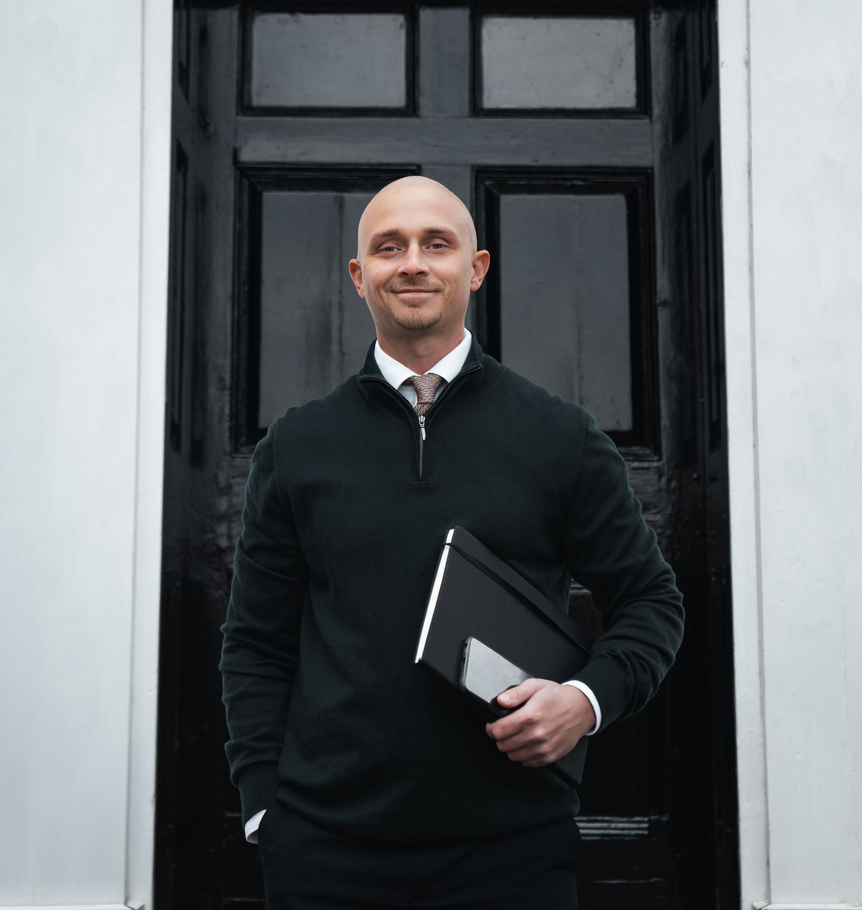 Man standing in front of a black door, holding a folder and smiling