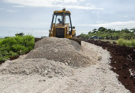 A bulldozer is moving a pile of gravel on a dirt road.