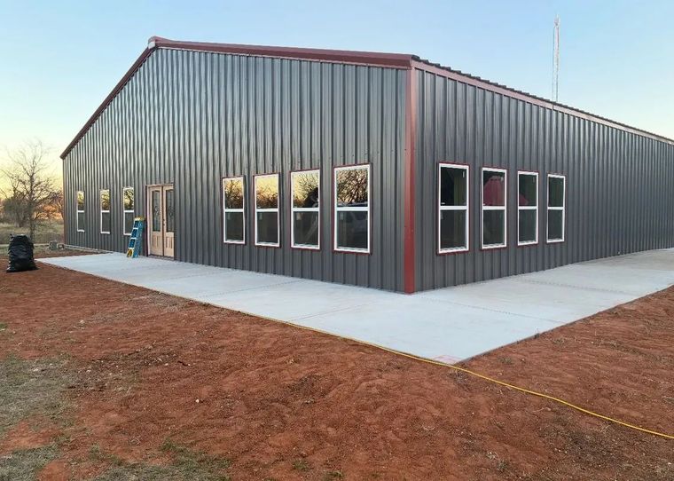 Metal building with gray siding, red trim, and rows of windows on a concrete slab