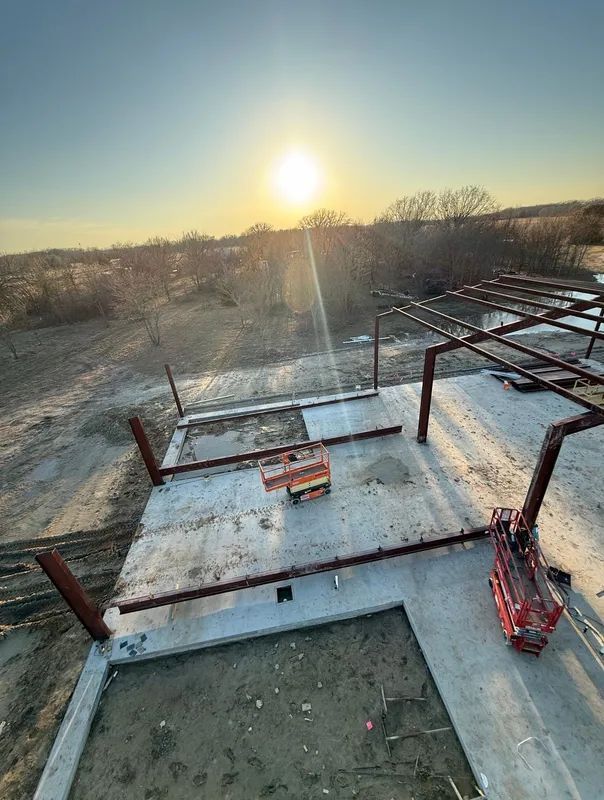 Sunset over a snowy rooftop construction site with steel framing and concrete slabs