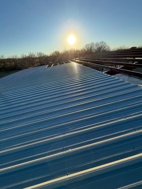 Snow-covered corrugated roof at sunrise with long shadows and bare trees in the background