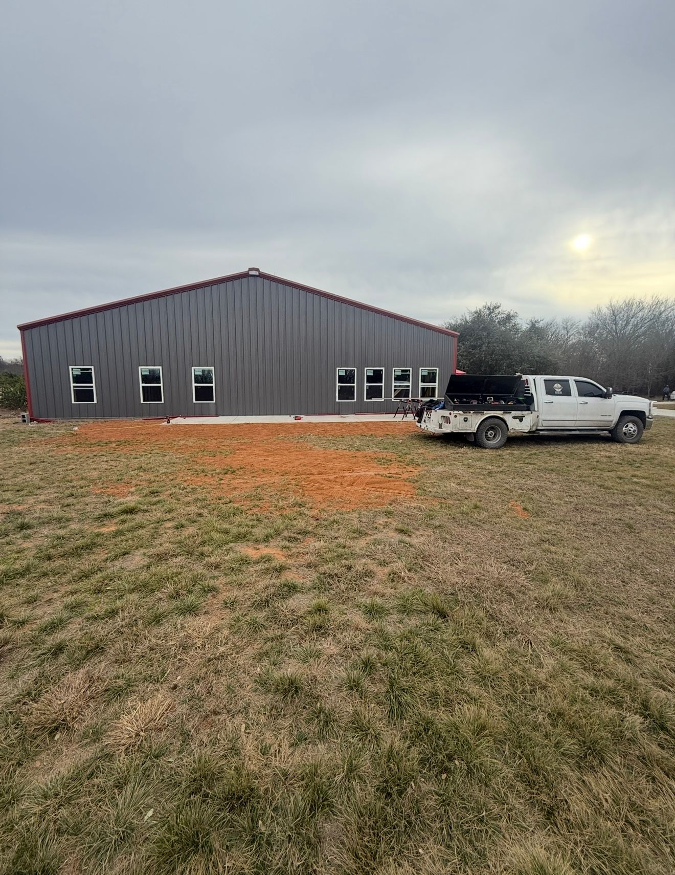 Gray metal building in a grassy field with a white pickup truck parked beside it under an overcast sky