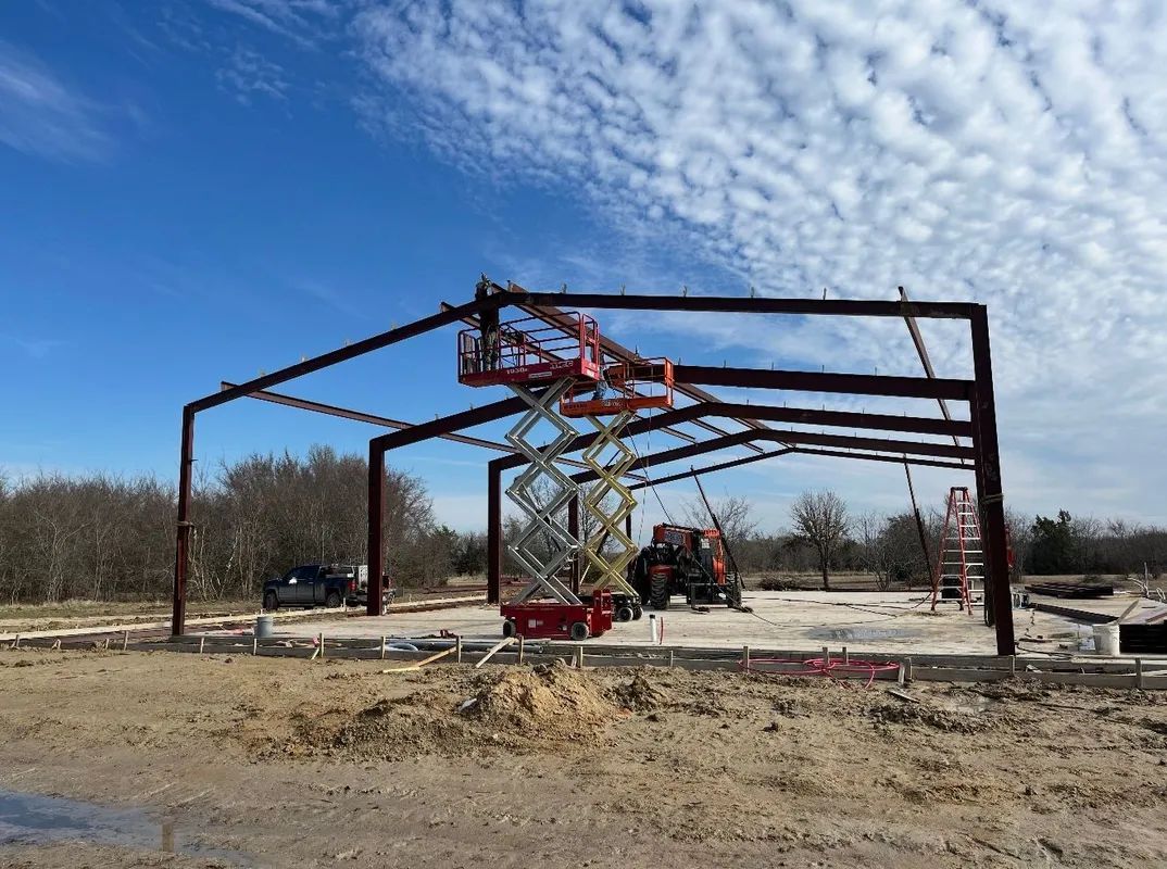 Steel frame of a building under construction, with a red crane against a cloudy blue sky.