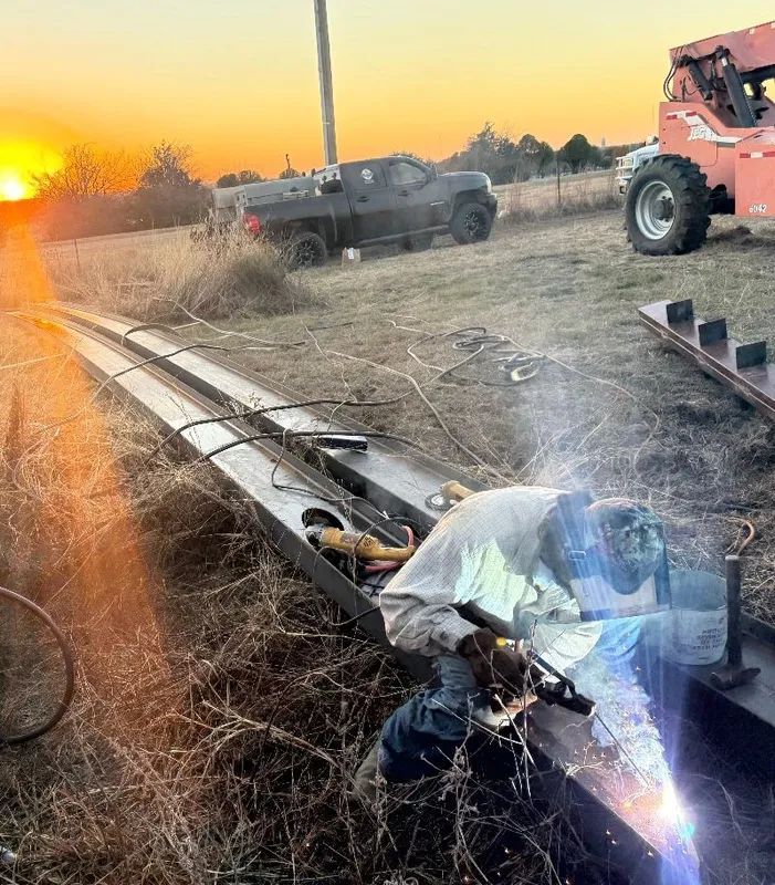 Wrecked vehicle on a dirt roadside at sunset, with smoke or steam rising and emergency truck nearby.