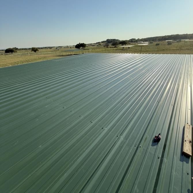 Green metal roof under construction in a rural field, with tools and a wooden plank at the edge