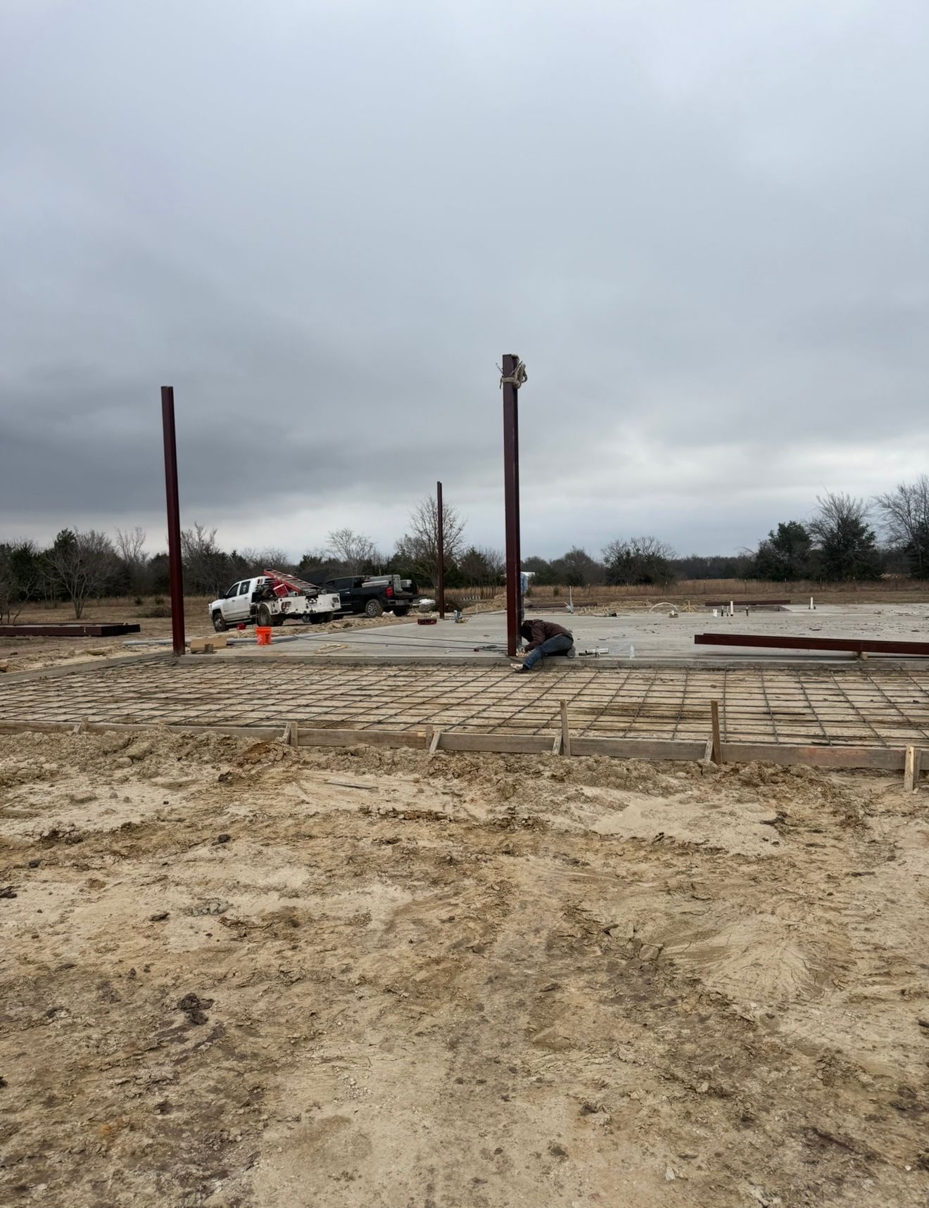 Bare construction site with muddy ground, two steel posts, and cloudy gray sky.
