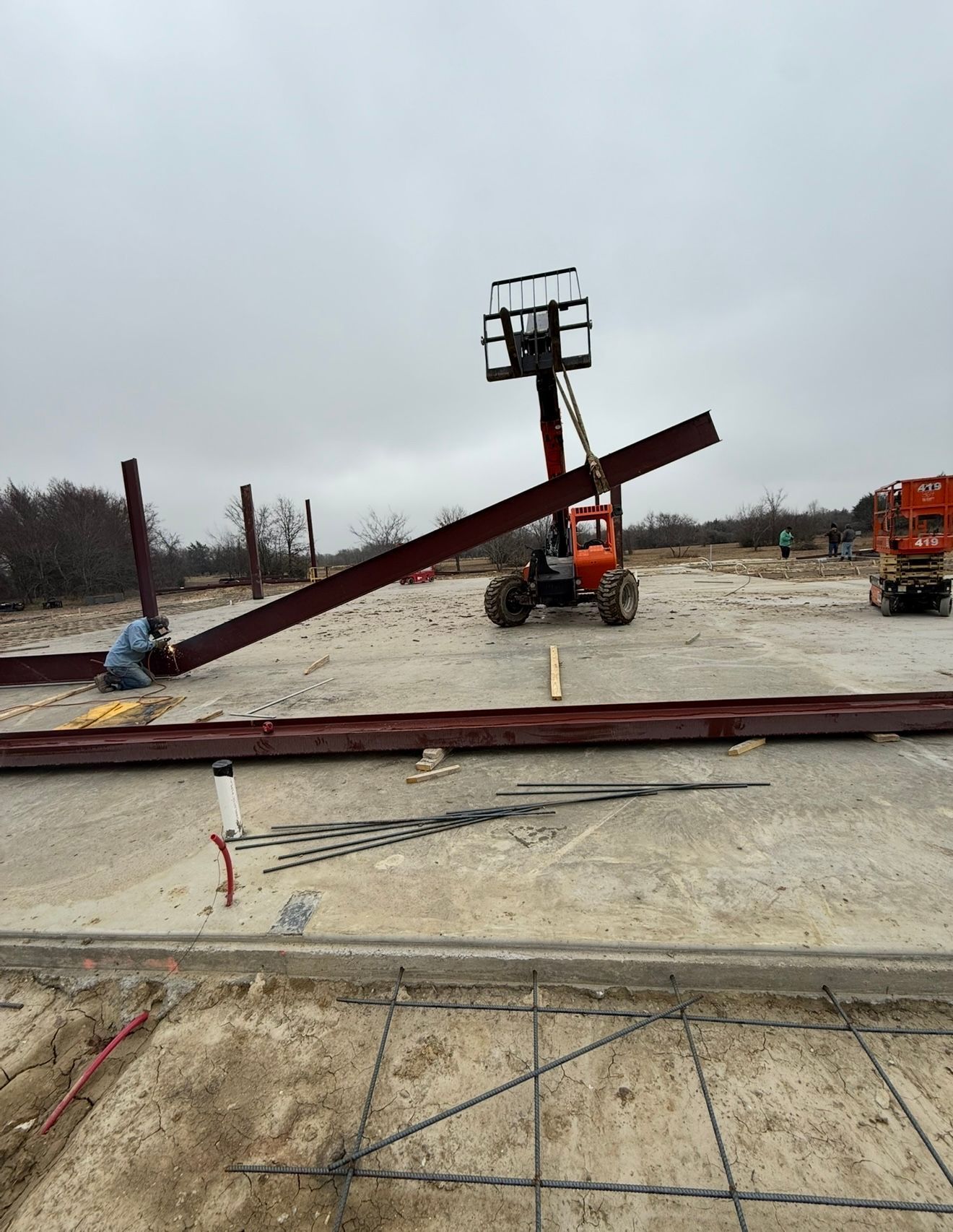 Damaged red steel beam leaning in a muddy industrial site with heavy equipment in the background