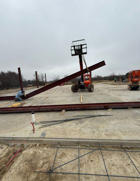 Damaged red boom lift collapsed on a muddy construction site under an overcast sky.