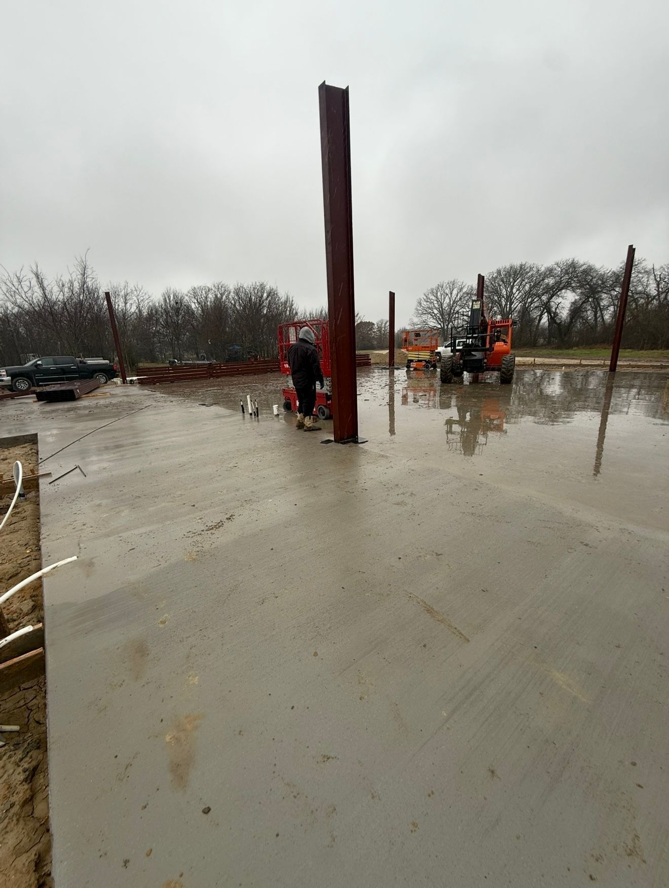 Workers erecting tall steel posts on a wet construction site during rain