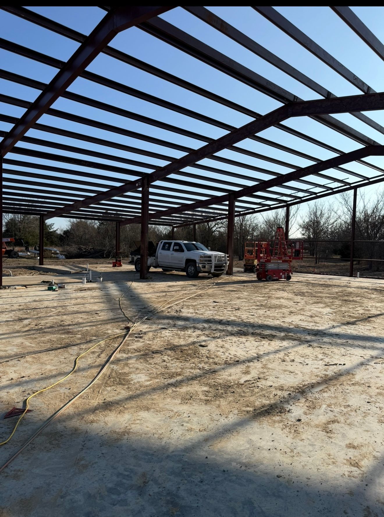 Steel frame building under construction on a sandy site, with a pickup truck and equipment inside.