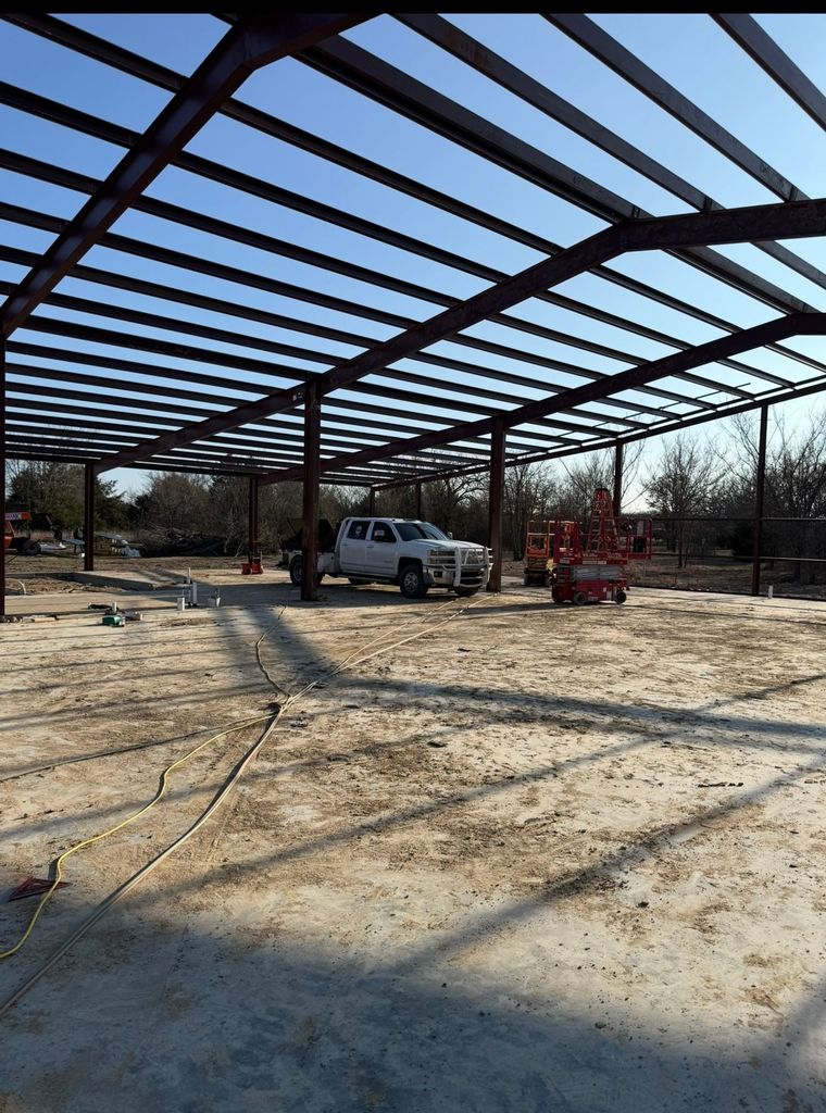 Steel frame building under construction with a white truck and red lift on a dirt lot