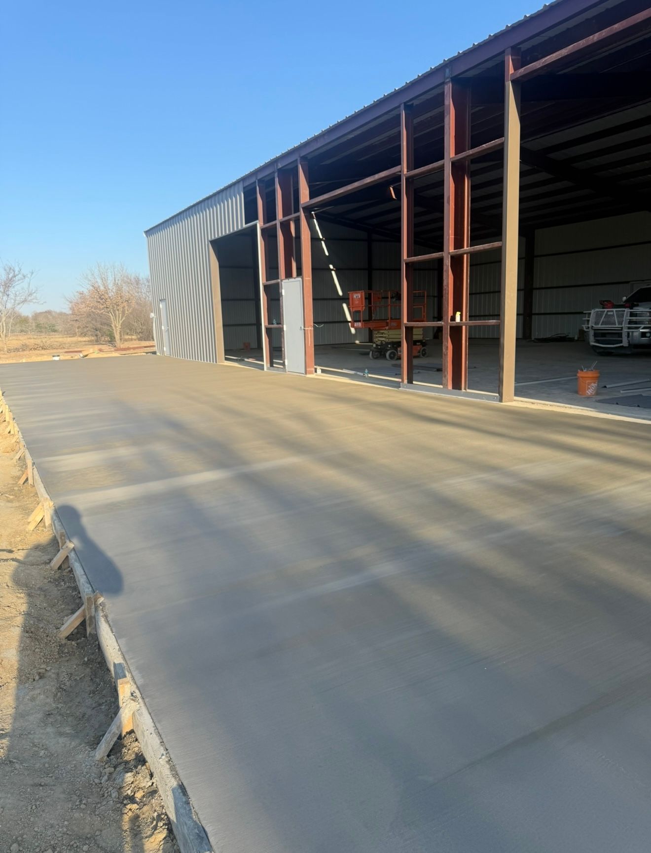 Empty concrete driveway beside an open metal storage shed with red support posts