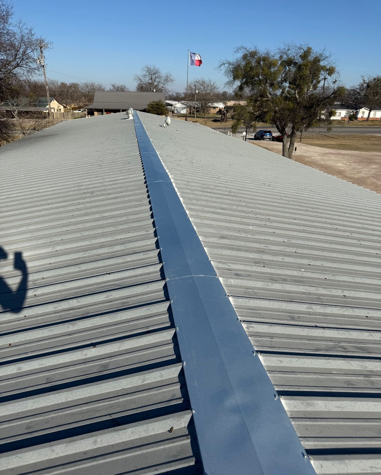 Rooftop metal walkway leading toward a distant American flag under a clear blue sky.