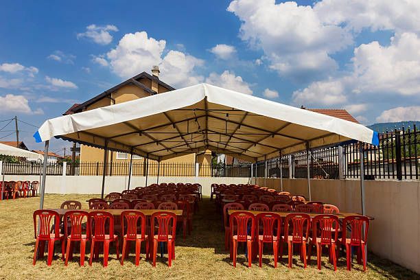 Outdoor event setup with red chairs and tables under a white tent, blue sky in the background.
