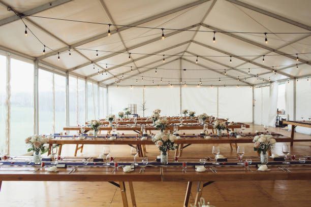 Wedding reception tent with long wooden tables set for guests, string lights overhead.