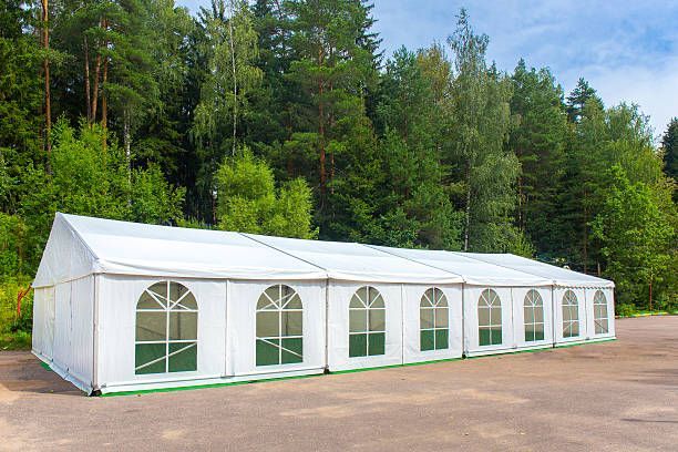White tent with arched windows set against a backdrop of green trees.