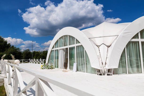 White tent structure on a deck with arched windows, bright blue sky, and clouds.