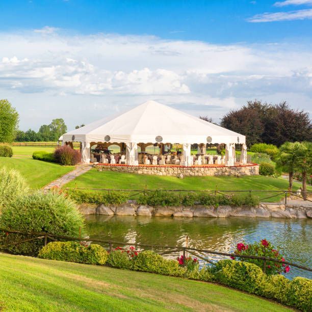 White tent set up on a grassy hill overlooking a pond with blue sky in the background.