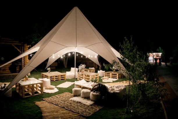 Outdoor lounge area under a white tent at night, with pallet furniture, rugs, and string lights.