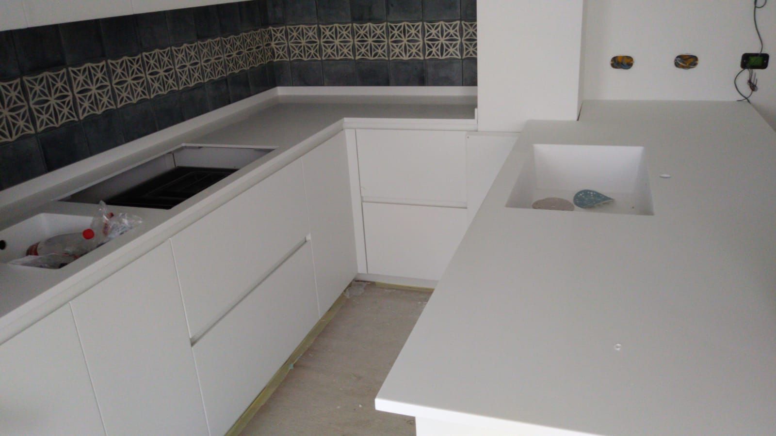 Cucina bianca con ripiani in quarzo, elettrodomestici da incasso e paraschizzi piastrellato blu.