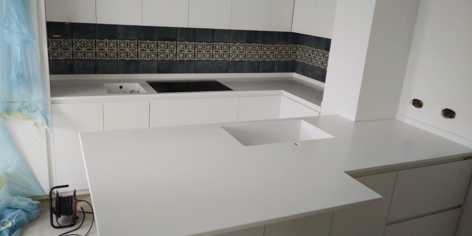 Piano di lavoro bianco per la cucina con piano cottura nero e paraschizzi decorativo.