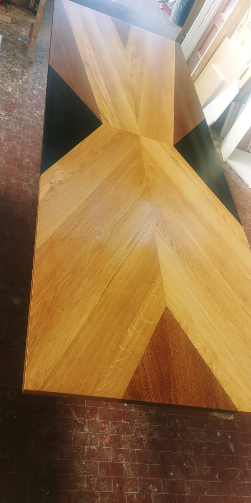 Tavolo in legno con motivi a spina di pesce e triangolari in varie tonalità di legno e nero.